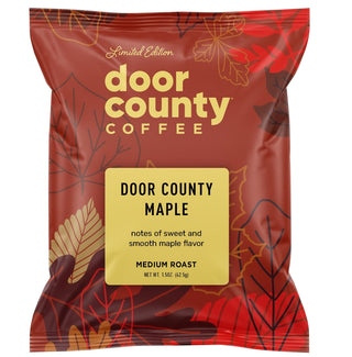 A red Door County Coffee bag labeled Door County Maple, with decorative leaf illustrations and a yellow label panel. Large text above and below the bag reads 'MAKE THE PERFECT POT' and 'Each 1.