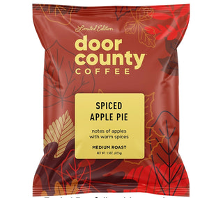 A red Door County Coffee bag labeled 'Spiced Apple Pie' with decorative leaf graphics and a yellow label panel, shown on a white background with promotional text above and below.