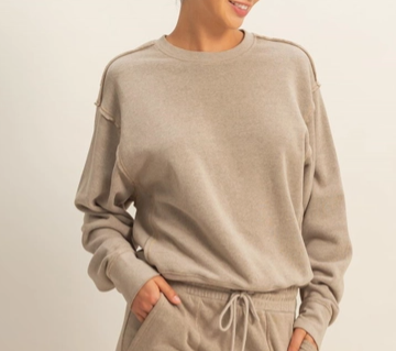 A person wearing a light taupe crewneck sweatshirt and matching drawstring sweatpants against a plain light background.